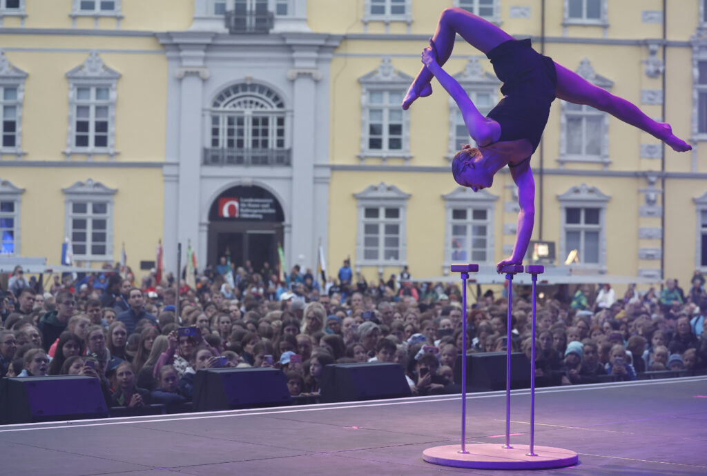 Eine Artistin balanciert in akrobatischer Pose auf Handstäben vor begeistertem