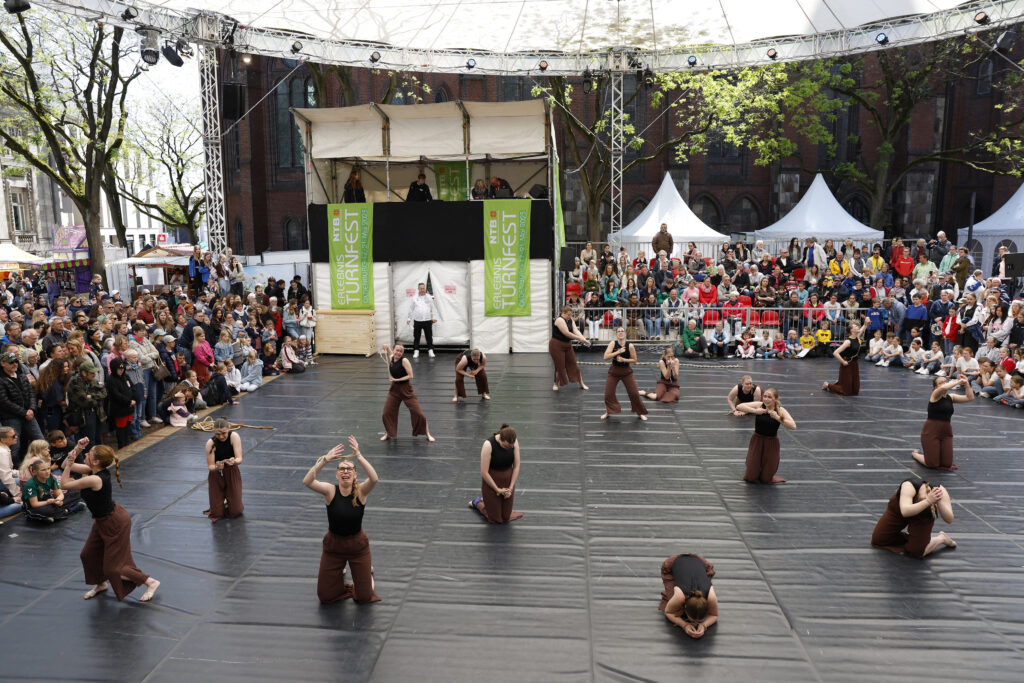 Eine Tanzgruppe performt auf einer Bühne vor zahlreichem Publikum.