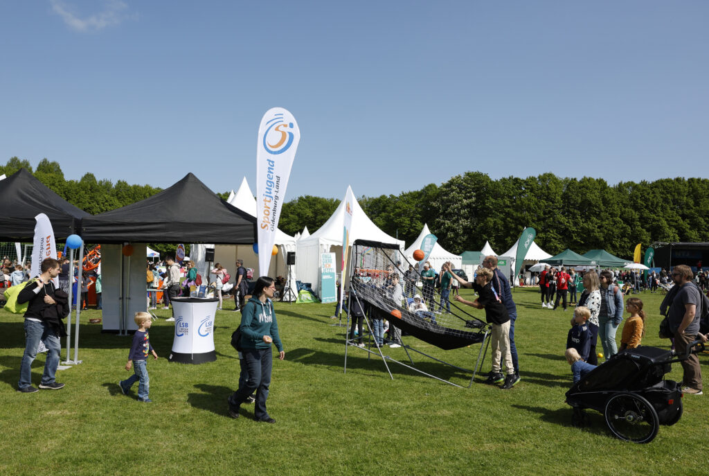 Besucher probieren Sport- und Spielstationen auf einer großen Wiese aus.