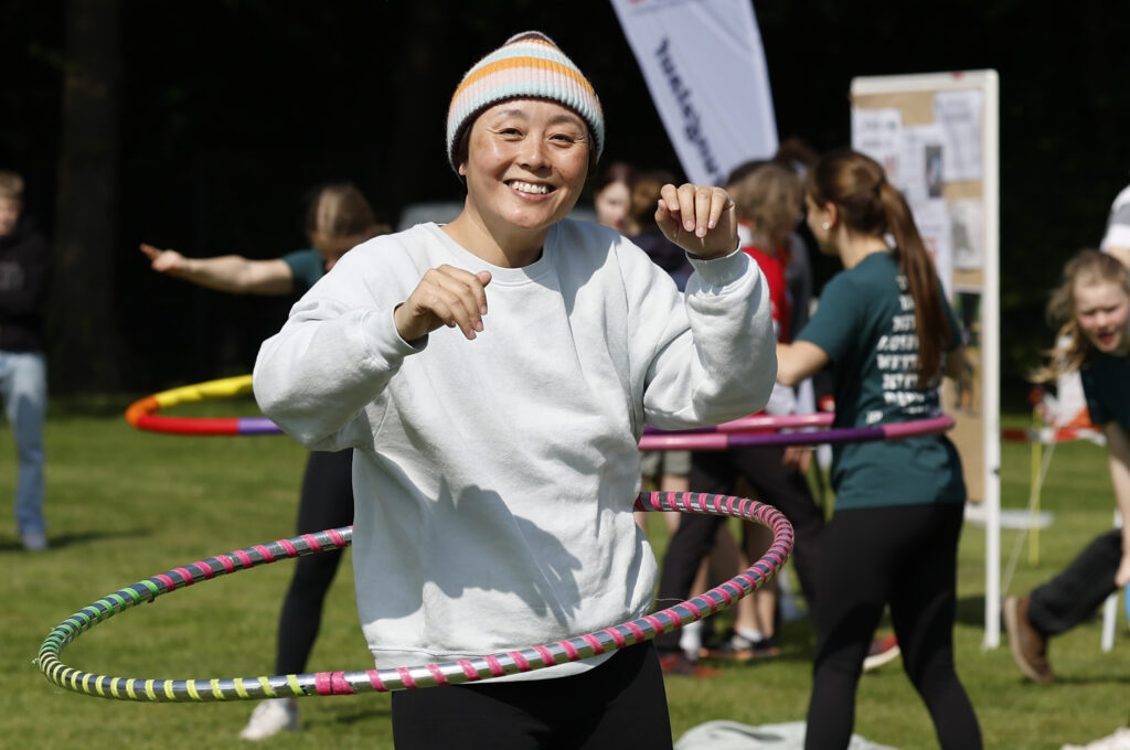 Eine Frau lächelt beim Hula-Hoop-Training auf einer Wiese.