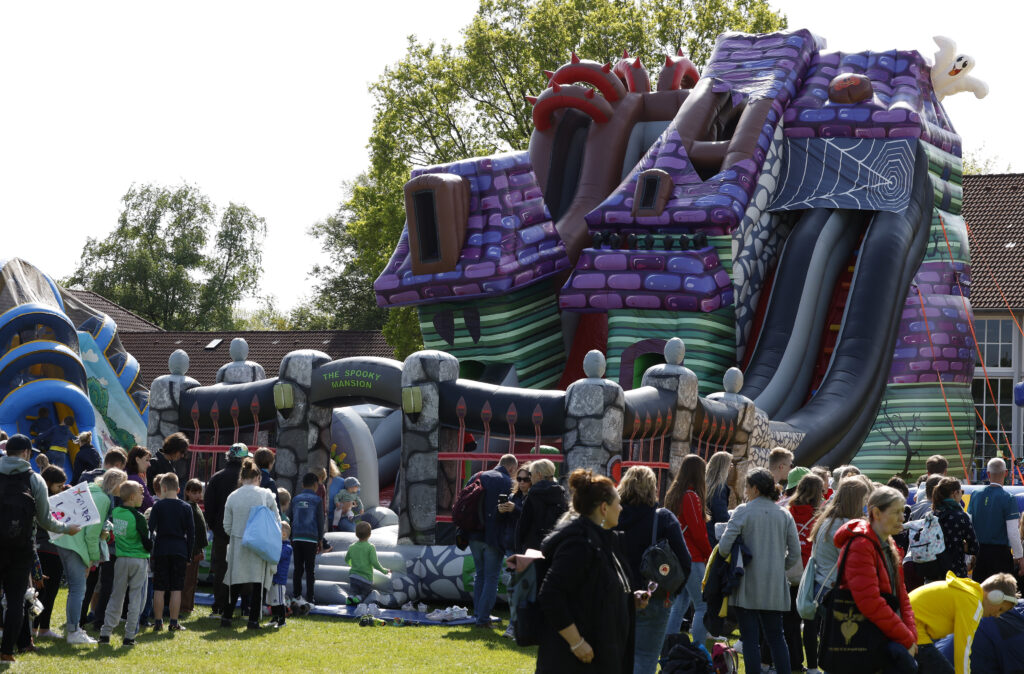 Viele Familien stehen vor einer großen, bunten Hüpfburg auf einer Wiese.