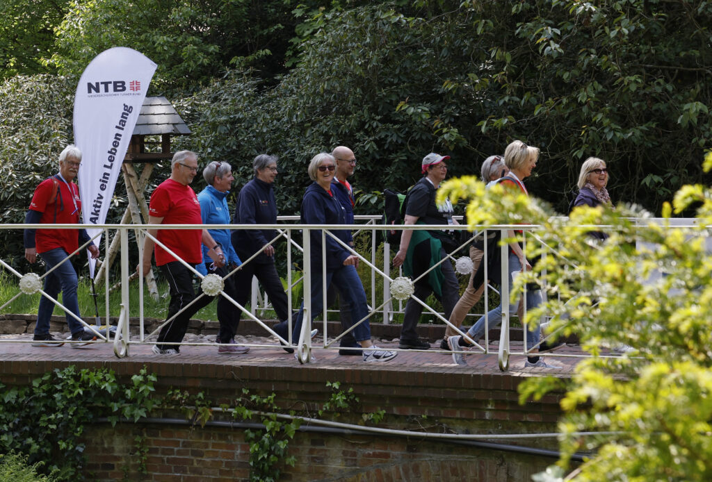 Eine Gruppe Erwachsener spaziert gut gelaunt über eine Brücke im Grünen.