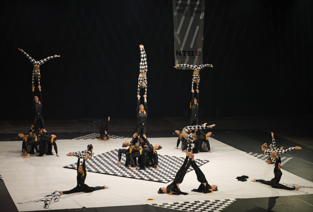 Mehrere Akrobatikgruppen präsentieren synchron anspruchsvolle Hebefiguren auf einer Bühne.