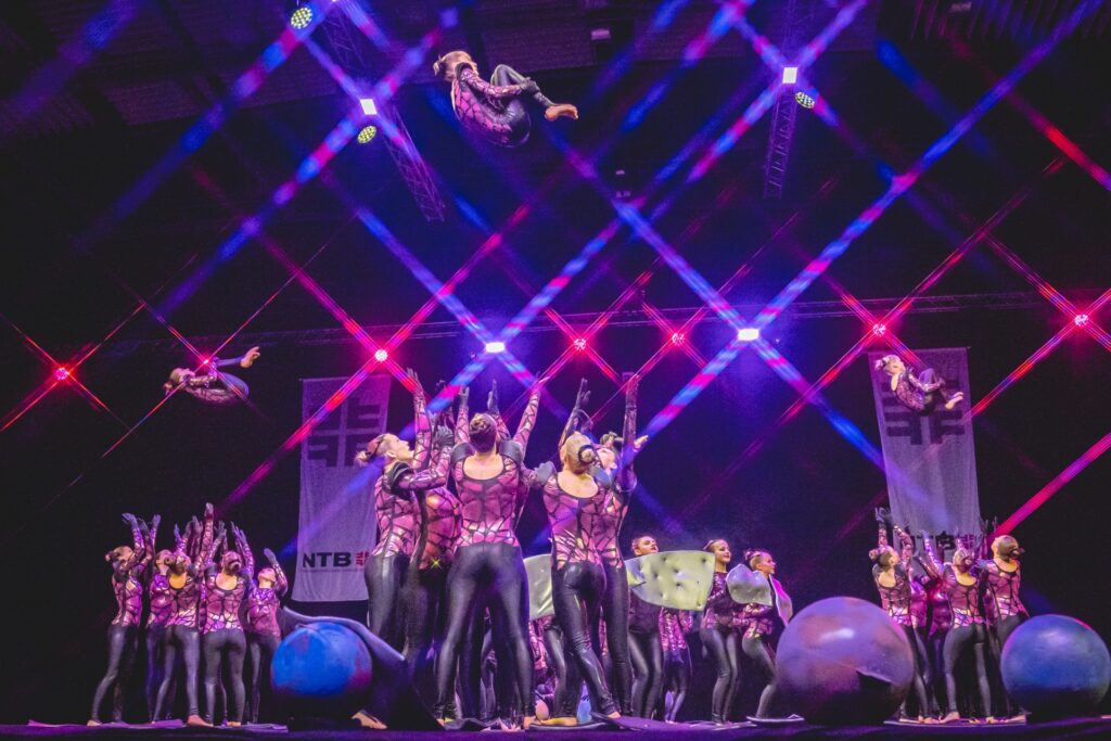 Showakrobatikgruppe Green Spirits führt eine akrobatische Choreografie auf einer beleuchteten Bühne mit bunten Lichteffekten auf.