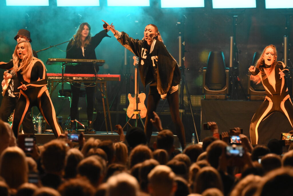 Live-Band und Tänzerinnen sorgen für ausgelassene Stimmung vor einer dicht gefüllten Zuschauermenge.