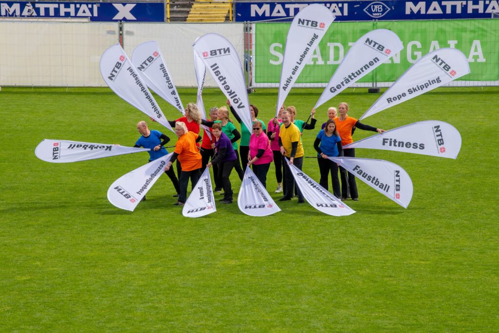 Sportgruppe hält Beachflags fächerförmig auf dem Stadionrasen