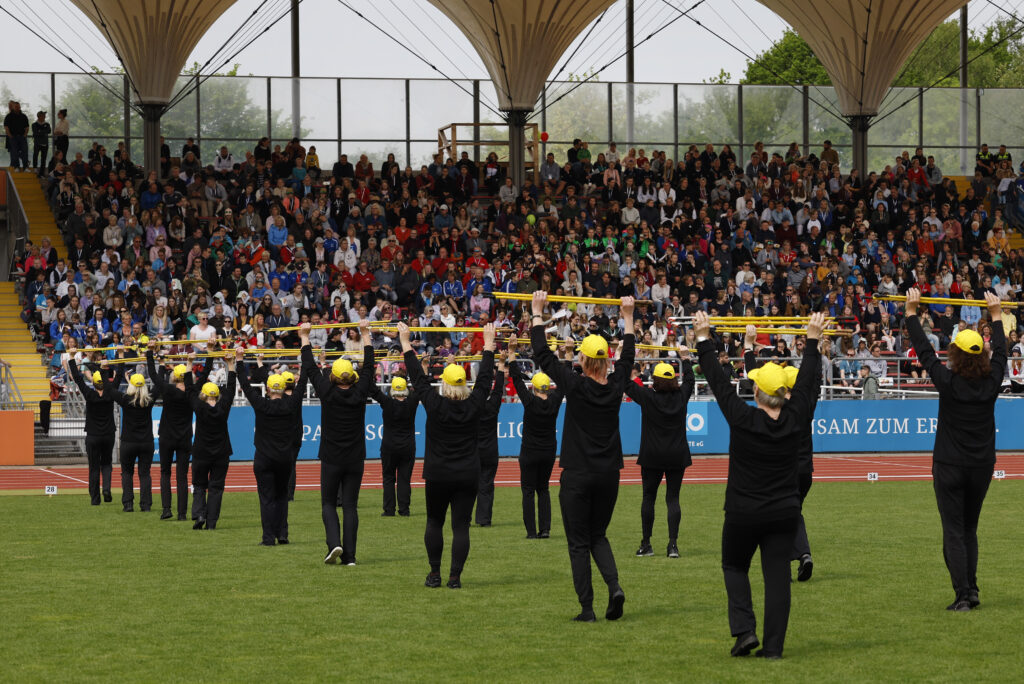 Fitnessgruppe mit gelben Pompons vor voll besetzter Stadiontribüne
