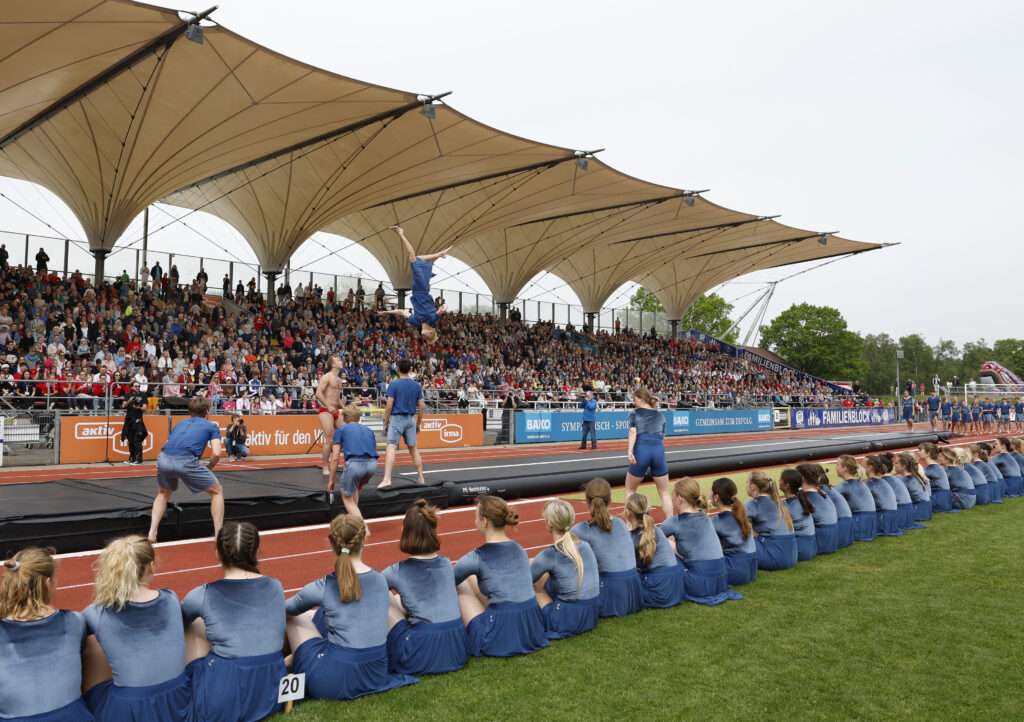 Große Turnshow im Stadion mit Akrobatinnen auf einer AirTrack-Bahn vor voll besetzten Zuschauerrängen
