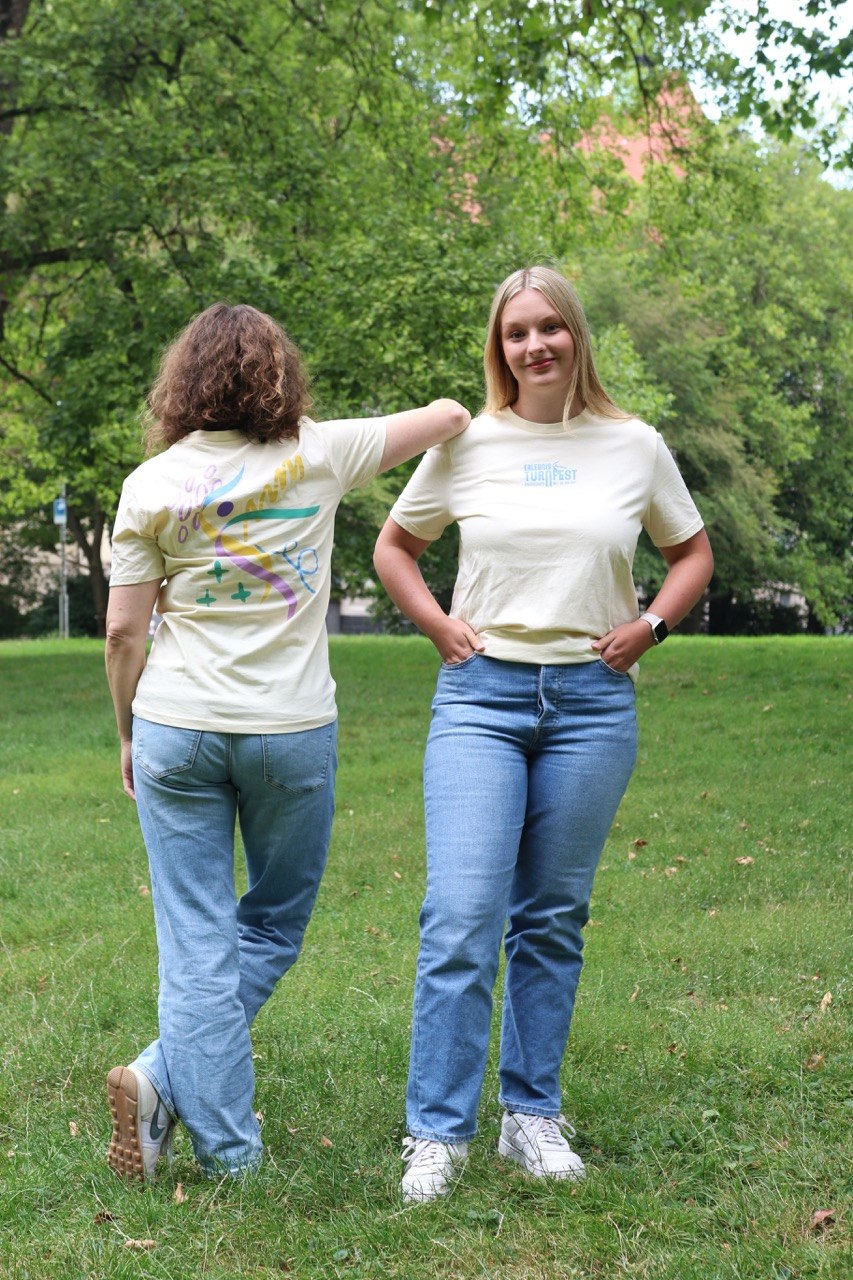 Zwei Personen zeigen Vorder- und Rückseite des pastellgelben Turnfest-T-Shirts