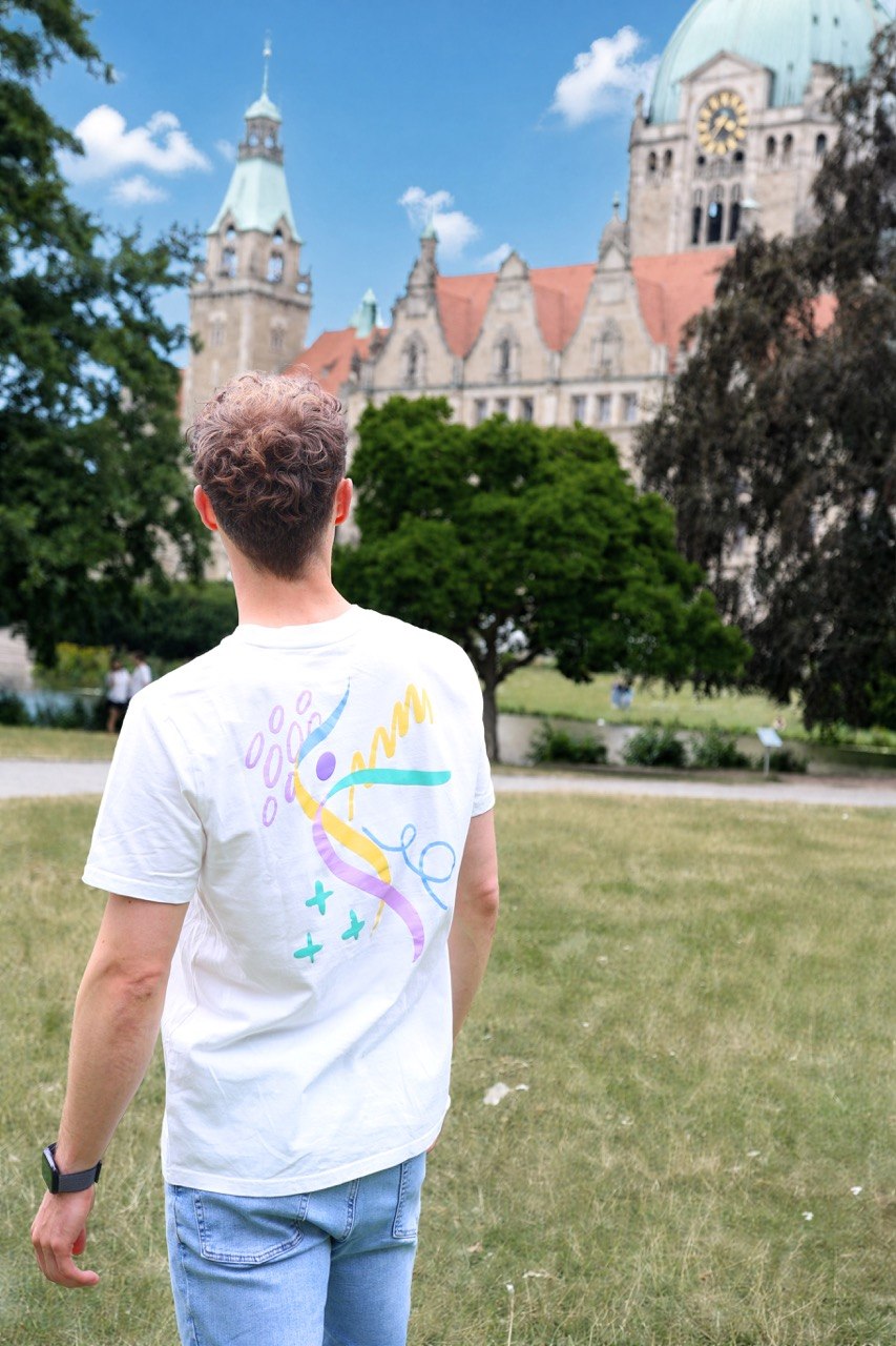 Person zeigt den großen Rückenprint des weißen Turnfest-T-Shirts vor dem Braunschweiger Rathaus