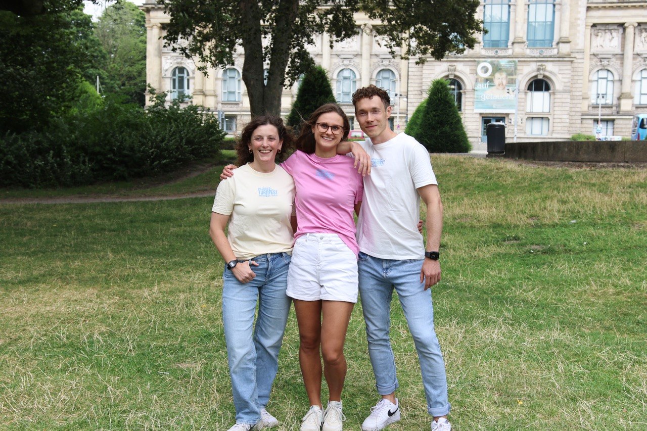Drei Personen tragen die Turnfest-T-Shirts in Pastellgelb, Pink und Weiß