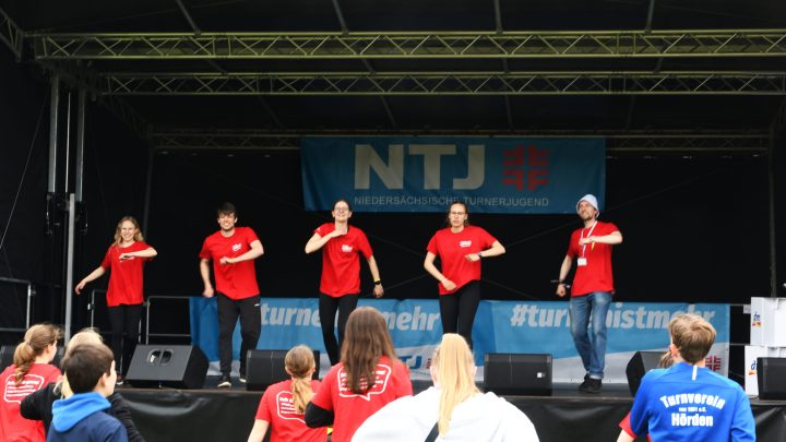 5 Personen im roten T-Shirt stehem auf der NTJ-Bühne und machen einen Tanz
