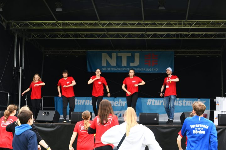 5 Personen im roten T-Shirt stehem auf der NTJ-Bühne und machen einen Tanz