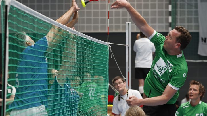 Indiacaspieler schlägt den Indiaca-Ball über das Netz, während ein Gegenspieler den Angriff blockt.