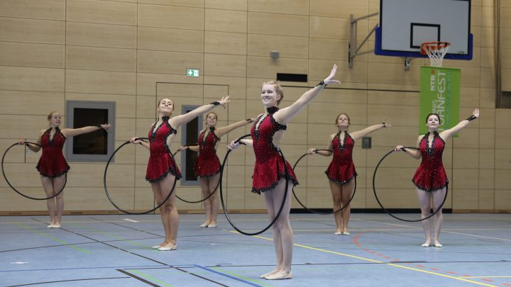Gymnastikgruppe präsentiert eine synchrone Reifen-Choreografie während eines Wettkampfs in der Sporthalle
