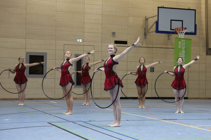 Gymnastikgruppe präsentiert eine synchrone Reifen-Choreografie während eines Wettkampfs in der Sporthalle