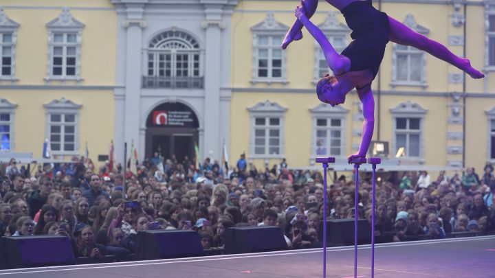 Eine Artistin balanciert in akrobatischer Pose auf Handstäben vor begeistertem