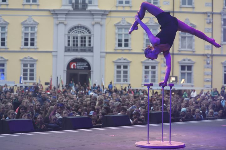 Eine Artistin balanciert in akrobatischer Pose auf Handstäben vor begeistertem