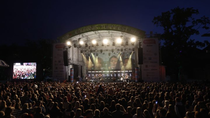 Große Open-Air-Bühne mit Lichtshow und jubelndem Publikum in der Dämmerung.