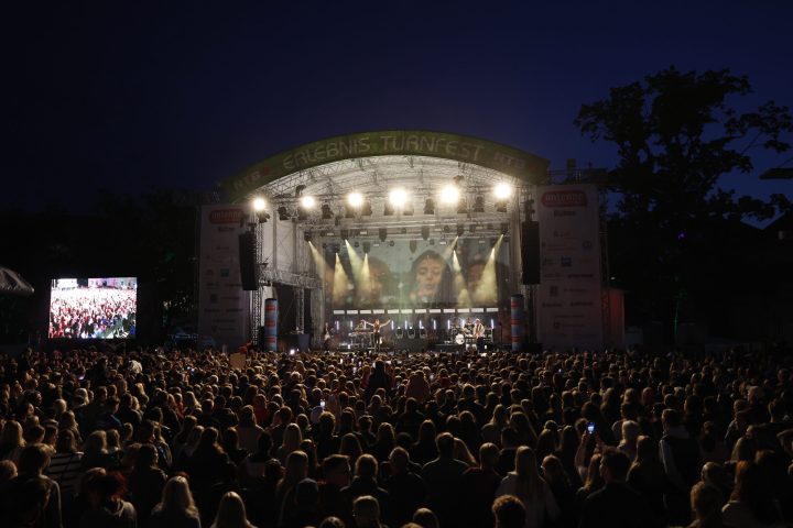 Große Open-Air-Bühne mit Lichtshow und jubelndem Publikum in der Dämmerung.