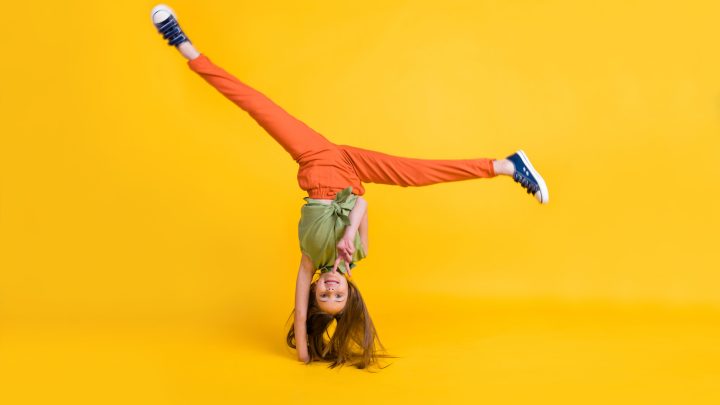 Full length body size photo little girl wearing casual clothes careless doing handstand isolated vivid yellow color background